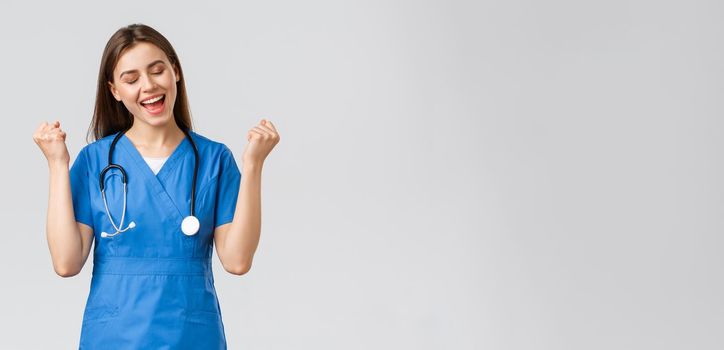 Medical workers, healthcare, covid-19 and vaccination concept. Happy cheerful female nurse, pretty enthusiastic doctor in blue scrubs, passed test, fist pump in rejoice, smiling relieved.