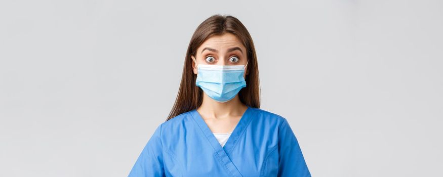 Covid-19, preventing virus, health, healthcare workers and quarantine concept. Surprised female nurse or doctor in blue scrubs and medical mask, staring shocked and excited at camera.