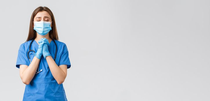 Covid-19, preventing virus, health, healthcare workers and quarantine concept. Hopeful female nurse or doctor in blue scrubs, medical mask, praying for lives of patients sick coronavirus infection.