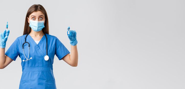 Covid-19, preventing virus, health, healthcare workers and quarantine concept. Excited female nurse in blue scrubs, doctor in clinic holding syringe and ampoule with coronavirus vaccine.