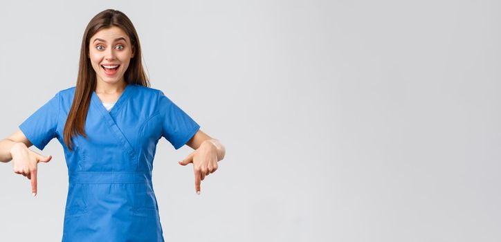 Healthcare workers, prevent virus, covid-19 test screening, medicine concept. Excited happy attractive nurse or doctor in blue scrubs, pointing fingers down, found great promo, showing banner.