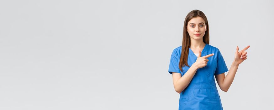 Healthcare workers, prevent virus, insurance and medicine concept. Young nurse or doctor in blue scrubs pointing fingers right, recommend banner or promo for clinic patients.