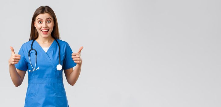 Medical workers, healthcare, covid-19 and vaccination concept. Enthusiastic and upbeat female nurse, doctor in blue scrubs, think wonderful idea, show thumbs-up in approval.