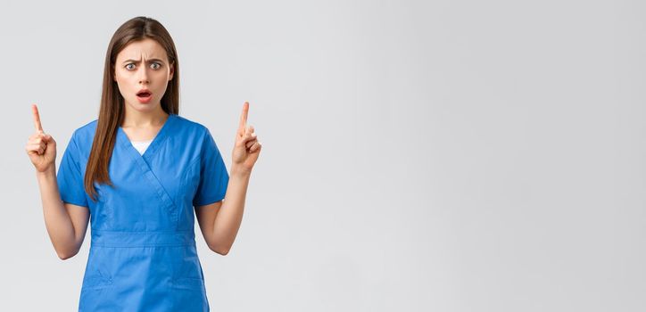 Healthcare workers, prevent virus, insurance and medicine concept. Oh gosh what this. Shocked and concerned nurse or doctor in blue scrubs, frowning upset, gasping pointing fingers up.