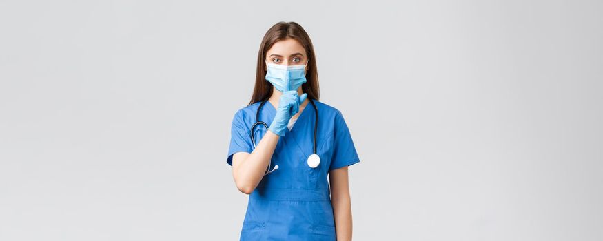 Covid-19, preventing virus, health, healthcare workers and quarantine concept. Keep voice down. Serious female nurse in blue scrubs, medical mask and gloves, shushing, press finger to lips.
