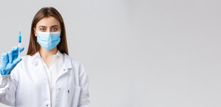 Covid-19, preventing virus, healthcare workers and quarantine concept. Determined professional doctor in medical mask and rubber gloves, showing syringe filled with coronavirus vaccine.