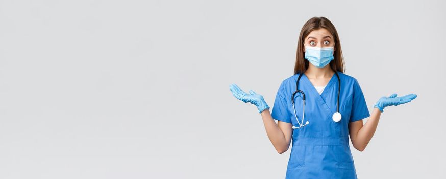 Covid-19, preventing virus, health, healthcare workers and quarantine concept. Surprised and excited female nurse or doctor in blue scrubs and medical mask, spread hands sideways amused.