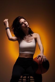 Teenage girl with basketball. Studio portrait on orange colored background.