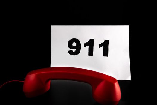 Call 911 and emergency call concept, text 911 on paper and phone isolated on black.