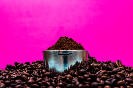 Coffee beans and portafilter with ground coffee in a composition on a pink background.