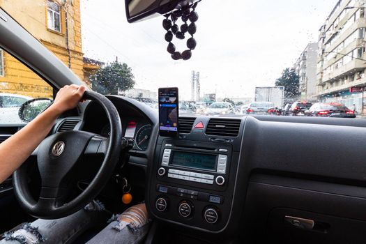 Using waze maps application on smartphone on car dashboard, Driver using maps app for showing the right route through the traffic of city on a rainy evening. Bucharest, Romania, 2020.