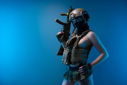 sexy girl soldier in a helmet, armed with an automatic rifle, in military clothes on a blue background