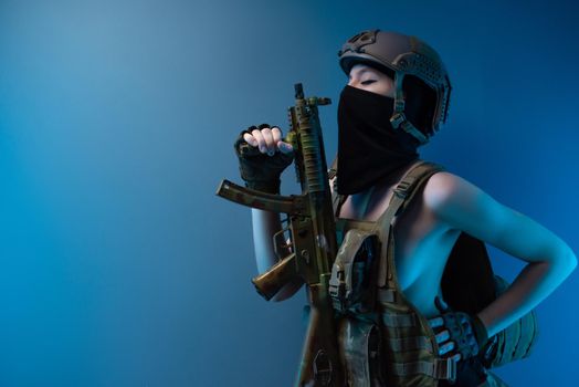 sexy girl soldier in a helmet, armed with an automatic rifle, in military clothes on a blue background