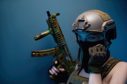 sexy girl soldier in a helmet, armed with an automatic rifle, in military clothes on a blue background