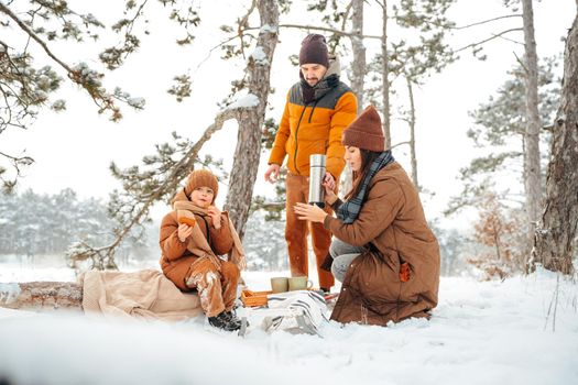 Happy family with cups of hot tea spending time together in winter forest, close up