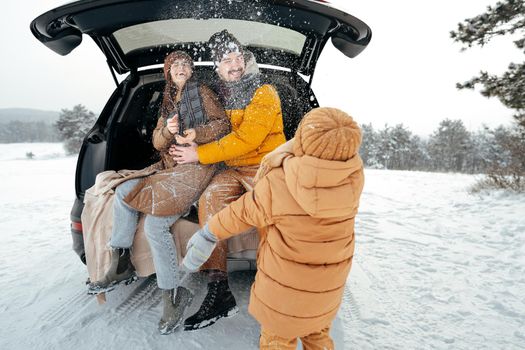 Lovely smiling couple sitting in car trunk in winter forest, close up