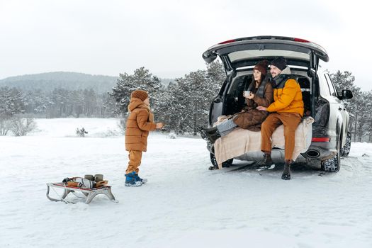 Winter portrait of a family sit on car trunk enjoy their vacation in snowy forest