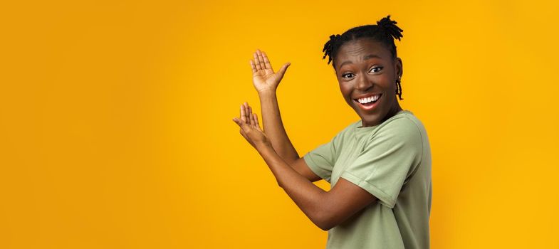 Cheerful Afro woman points to copy space in yellow studio, close up