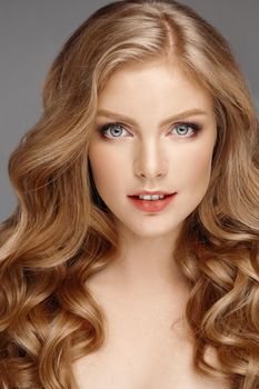 Studio fashion portrait of attractive sensual young woman with long wavy fair hair and blue eyes looking at camera. Natural beauty concept. Caucasian.