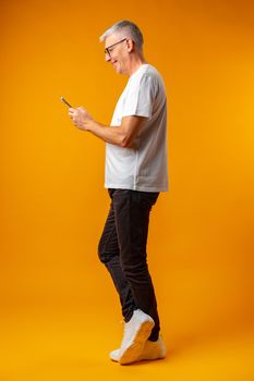 Senior smiling man using smartphone over yellow background, close up