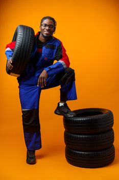 African american car service worker with car tyre against yellow background, close up