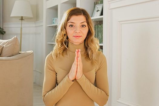 Portrait of a beautiful woman with blond hair, in the interior of the room, with folded hands on her chest, looks at the camera, smiles