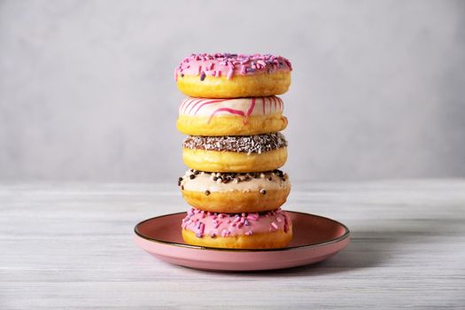 Stack of various colorful donuts on pink ceramic plate on gray background. Selective focus.