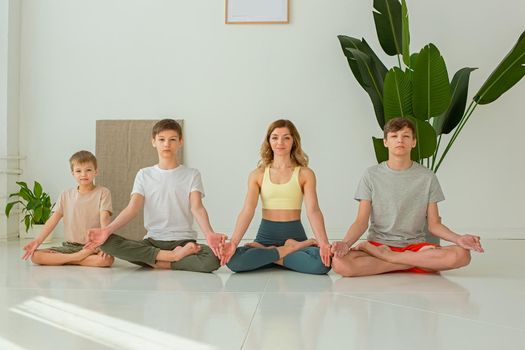 Beautiful family, a woman and three boys sit in the lotus position, in a bright room with green plants. Copy space