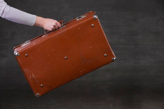 In hand is a brown retro suitcase on a gray background.