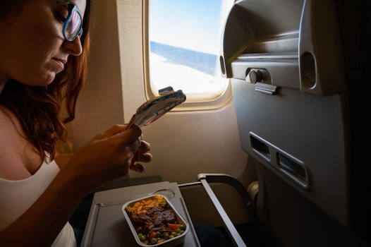 Caucasian woman flying in economy class and eating lunch from a tray table on board the plane