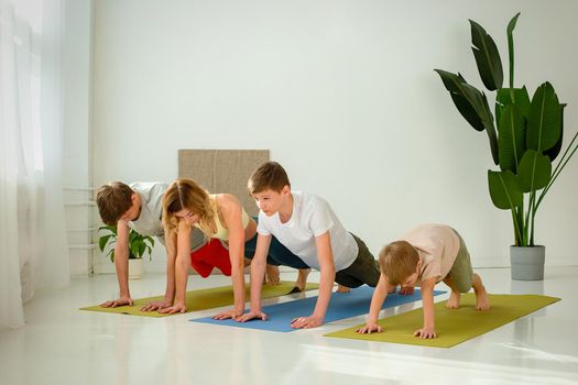a kid boy, two teenagers and a woman perform yoga exercises on mats, standing in a plank pose in daylight room