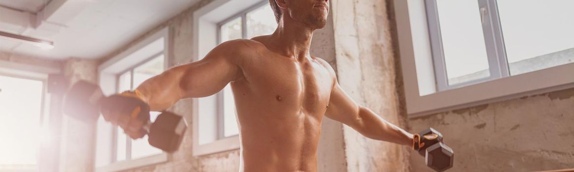 Young sporty man in workout gloves holding dumbbells and performing intensive workout in the fitness club