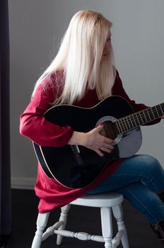 beautiful young blonde woman in a red dress with a black guitar, favorite hobby, music project. High quality photo