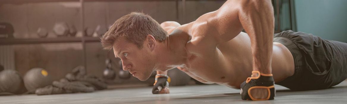 Strong muscular man in training gloves and shorts exercising actively and looking ahead in the fitness club