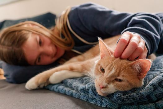 An Young Adolescent girl lying on a couch finds comfort by snuggling close to and petting her tabby cat