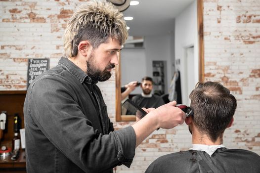 Man barber cutting hair of male client with clipper at barber shop. Hairstyling process. High quality photography