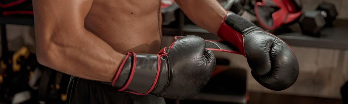 Close up of muscular man preparing for fight on boxing ring, wearing protective gloves for combat