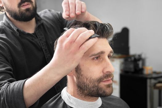 Man barber cutting hair of male client with clipper at barber shop. Hairstyling process. High quality photography