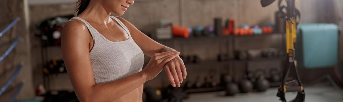 Young lady in sporty light top and leggings looking at her watch and preparing for workout