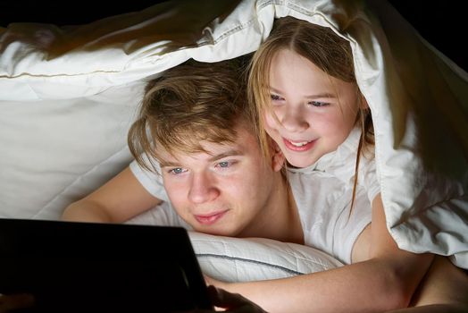 children play games on a tablet at night under a blanket, children watching video on tablet. communication through social networks. social media addiction.