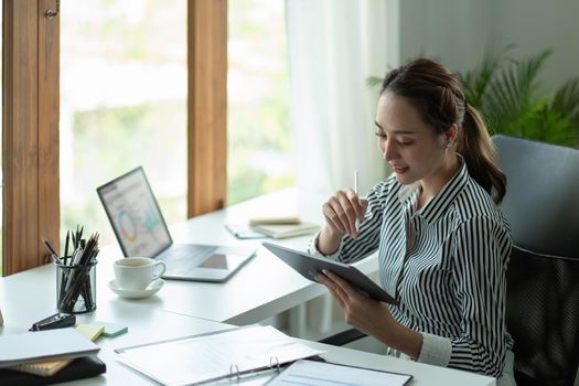 Attractive business asian woman using a digital tablet while sitting in workplace desk in an office