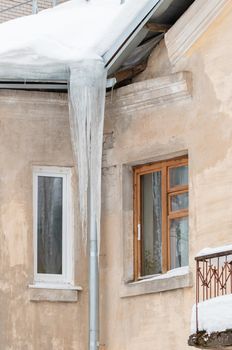 Fabulous ice icicles hang from a drainpipe at the edge of the roof. Against the background of the wall of an old brick house. Large cascades, even beautiful rows. Cloudy winter day, soft light.