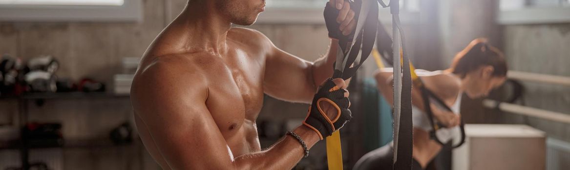 Young muscular man in workout gloves holding stretching tape and getting ready for training in the fitness club