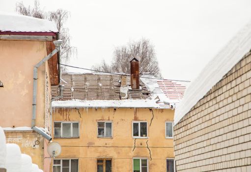 A brick house with a dismantled roof and hanging icicles on the edge. An old house against the backdrop of a gray sky. Large cascades, even beautiful rows. Cloudy winter day, soft light. UHD 4K.