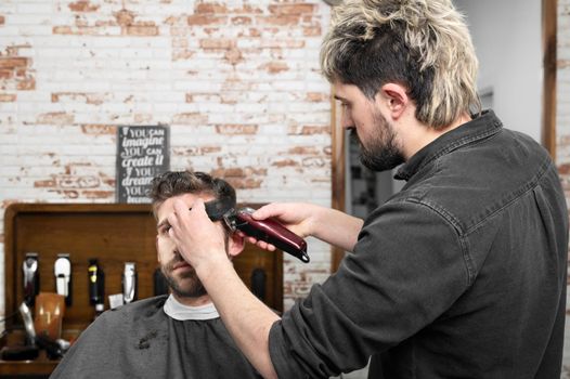 Man barber cutting hair of male client with clipper at barber shop. Hairstyling process. High quality photography