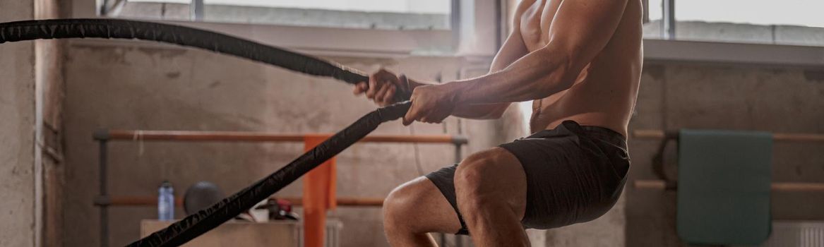 Cropped shot of fit sportsman in workout clothes doing cross-training exercise in modern gym club