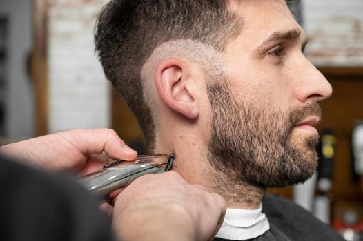 Man barber cutting hair of male client with clipper at barber shop. Hairstyling process. High quality photography