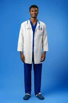 Confident black doctor posing over blue studio background, portrait