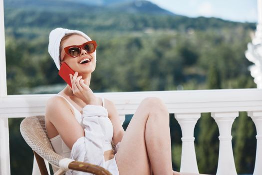 Portrait of young woman in a white shirt sits on the balcony with a phone Perfect sunny morning. High quality photo