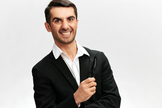 a man bares his teeth in a black business suit glasses in his hands an angry look light background. High quality photo